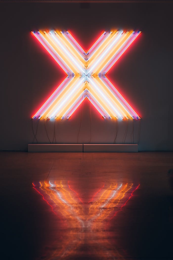 Vibrant neon X sign illuminating a dark room, reflecting on the floor.