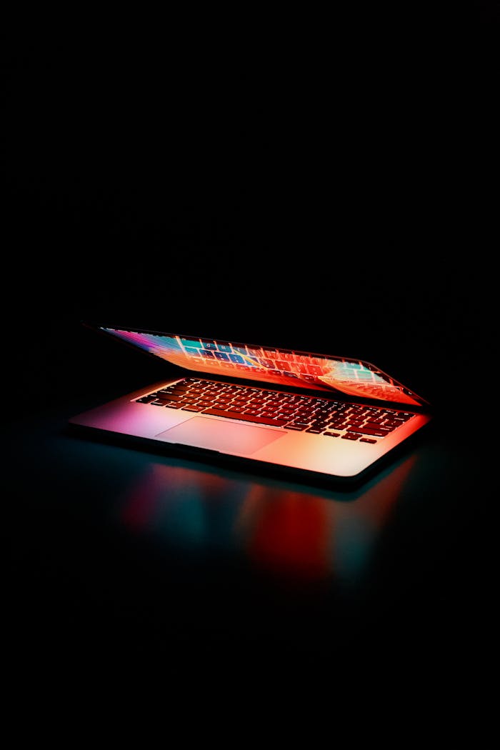about-03 Laptop partially opened, emitting vibrant multicolored lights in dark setting.