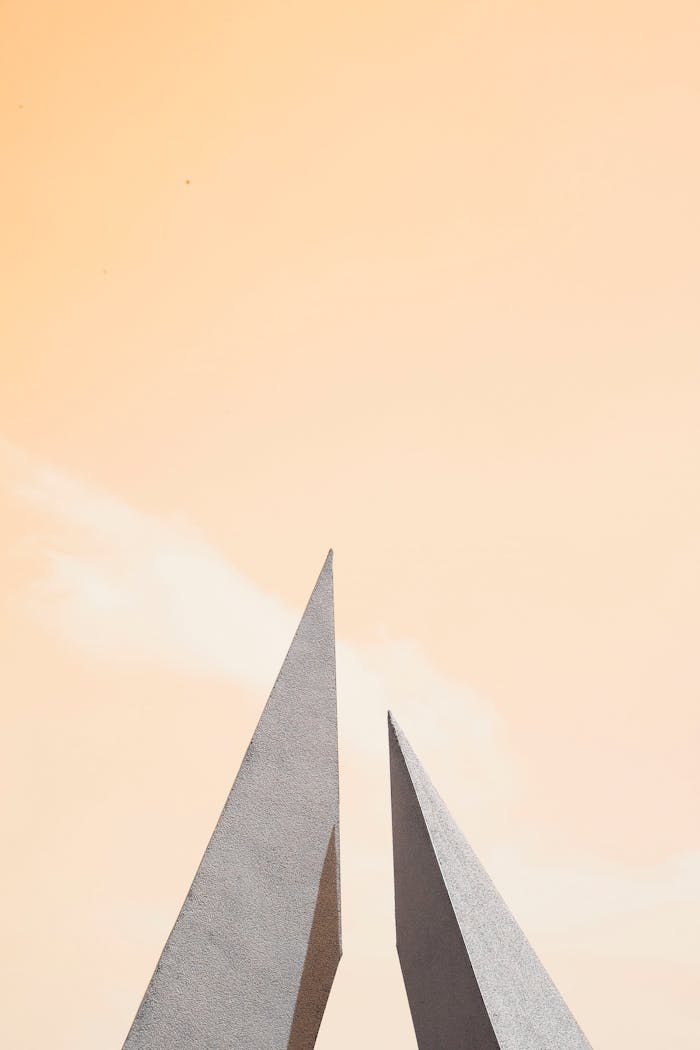 Modern minimalist architecture featuring sharp geometric forms against a soft pastel sky.